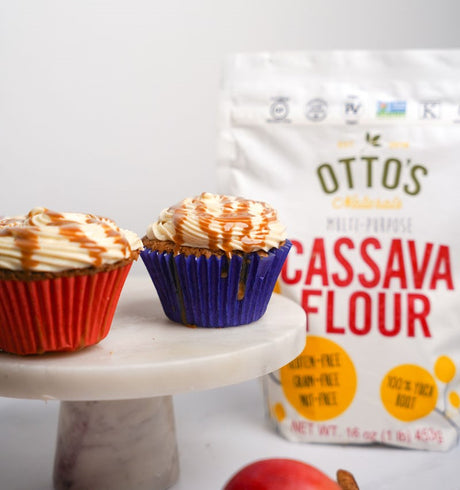 2 Caramel-Apple Cupcakes with caramel drizzle on cake stand. Otto's Naturals Cassava Flour Bag in background