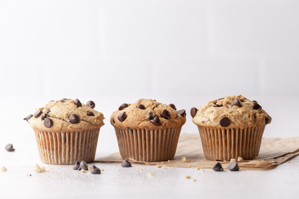 3 grain-free chocolate chip muffins with extra chocolate chips and parchment on counter