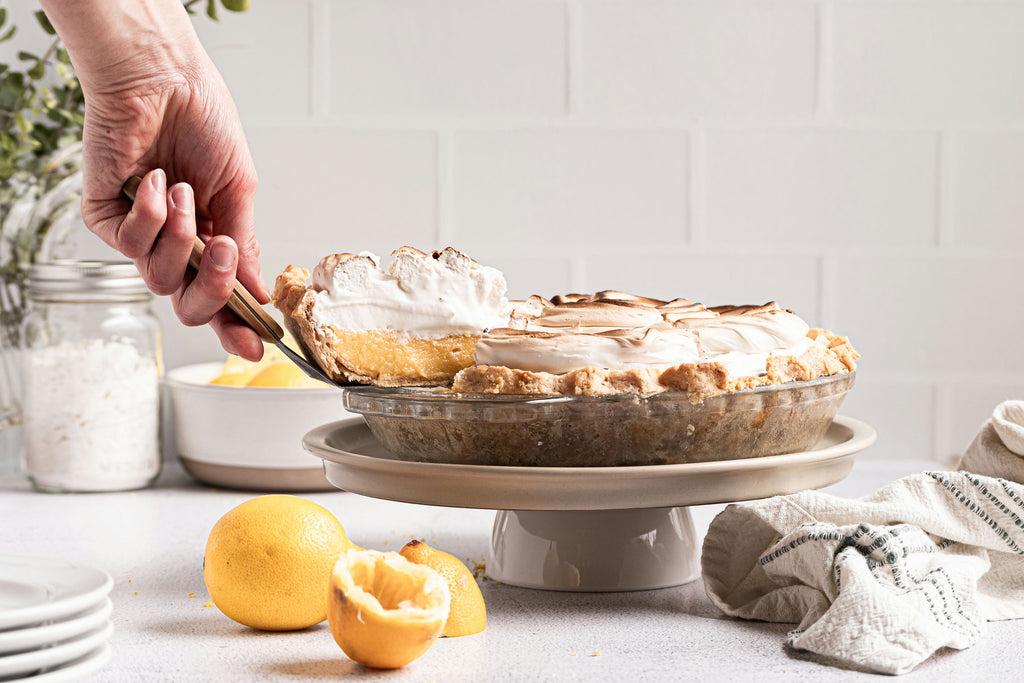 Grain-free lemon meringue pie on cake stand, with one slice being taken out.