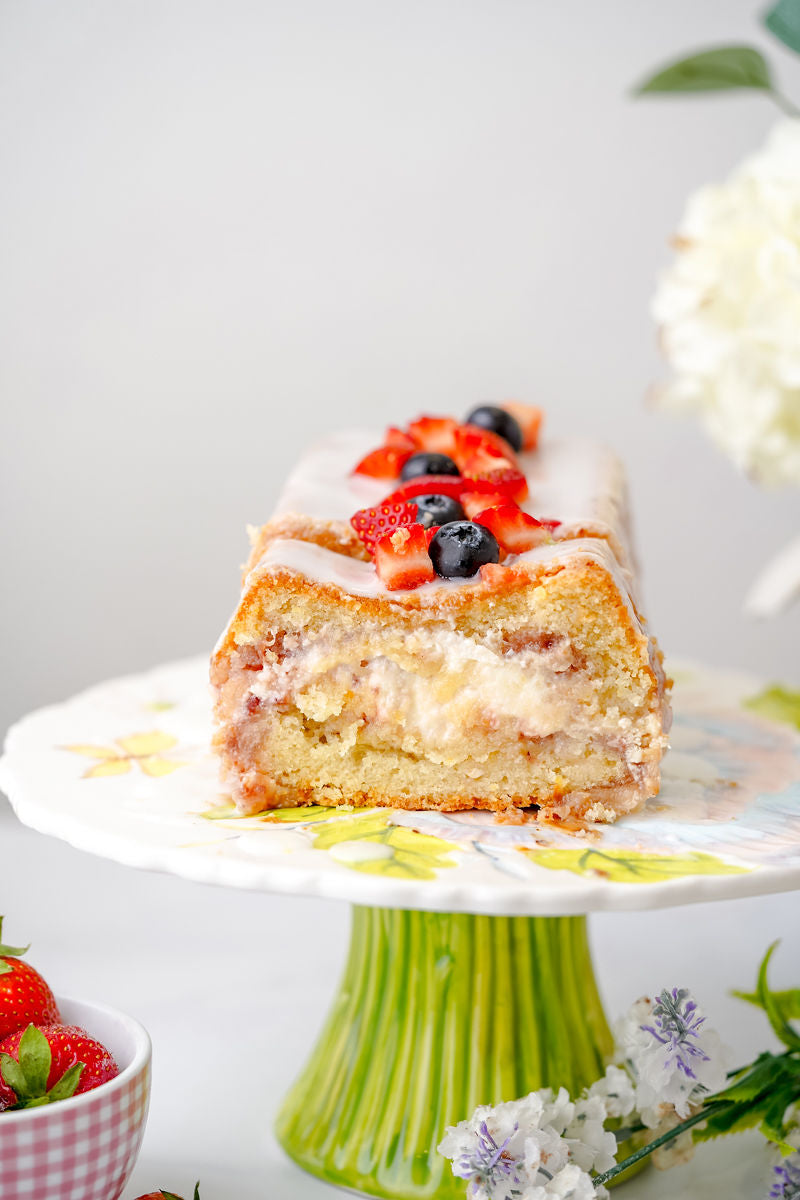 Grain-Free Strawberry Cream Cheese Pound cake with glaze and fresh berries on top. Sitting on cake stand