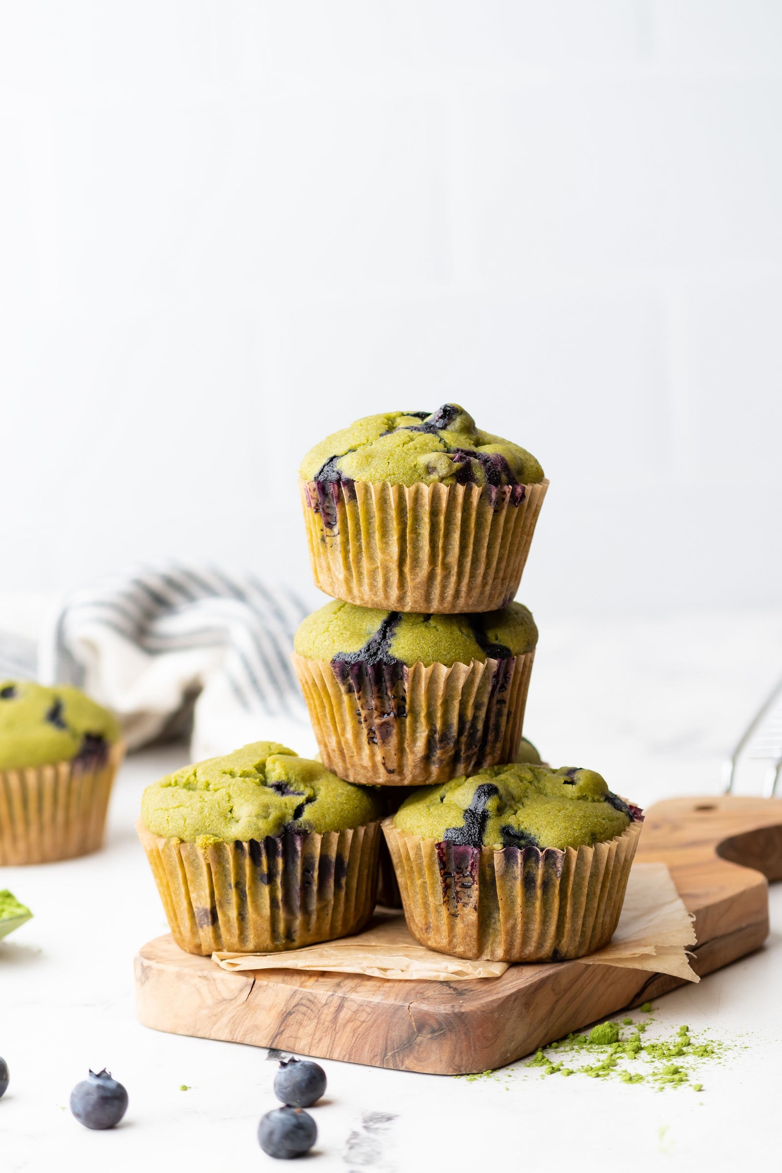 Grain-free matcha muffins with blueberries. Four muffins stacked on a wooden board.