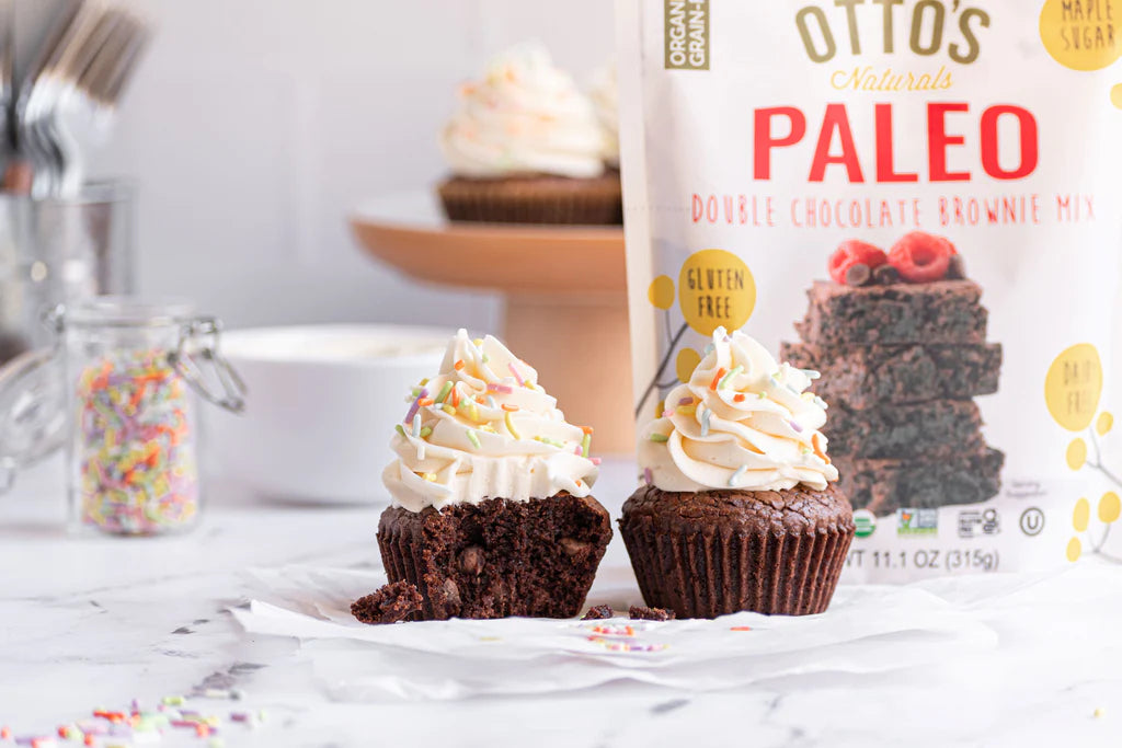2 grain-free chocolate brownie cupcakes with vanilla frosting. Otto's Naturals Paleo brownie mix in background