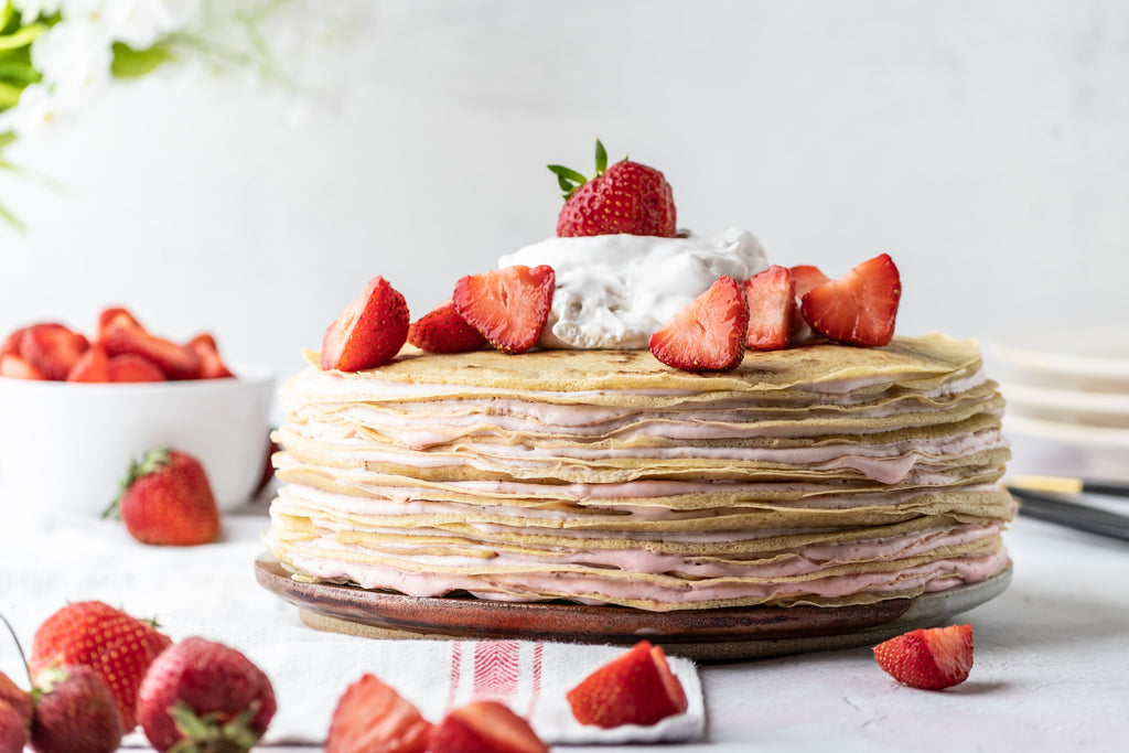 Strawberry crepe cake with strawberry cream and fresh berries and cream on top. 