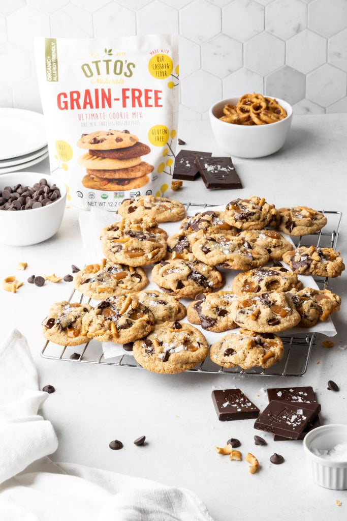 Rack of grain-free kitchen sink cookies, made with chocolate, caramel, and pretzels. Bag of Otto's Naturals grain-free ultimate cookie mix in background.